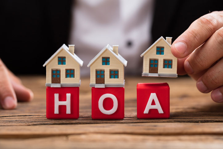 Homeowners association disputes concept. Person's hand placing house model over red HOA blocks on wooden desk.