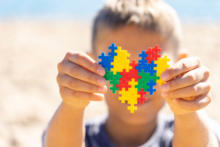 Special needs trusts. Boy hands holding colorful puzzle heart in front of his face